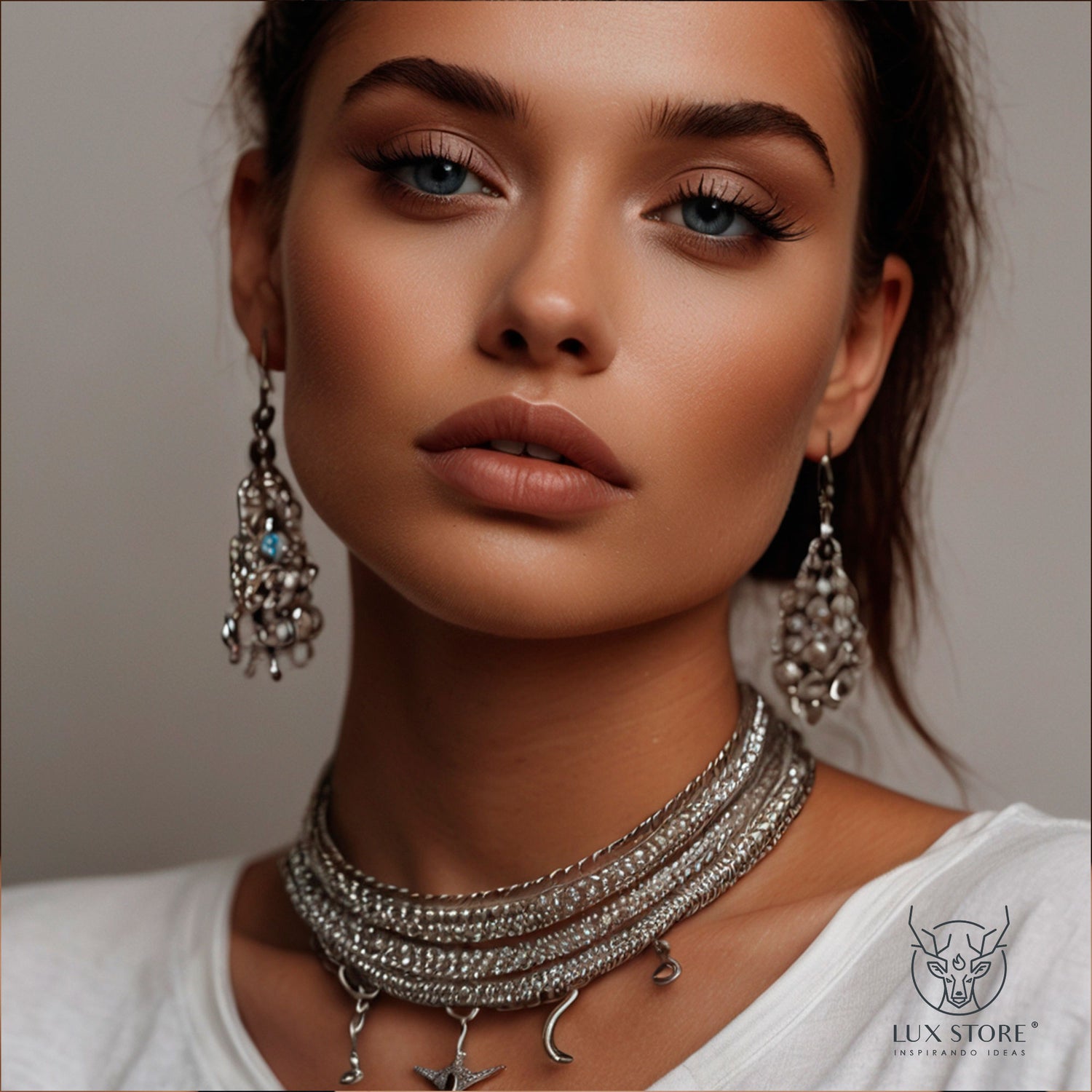 Primer plano de una modelo con un estilo sofisticado, luciendo un collar plateado de varias vueltas adornado con pequeños colgantes y unos pendientes colgantes decorados con detalles brillantes.
